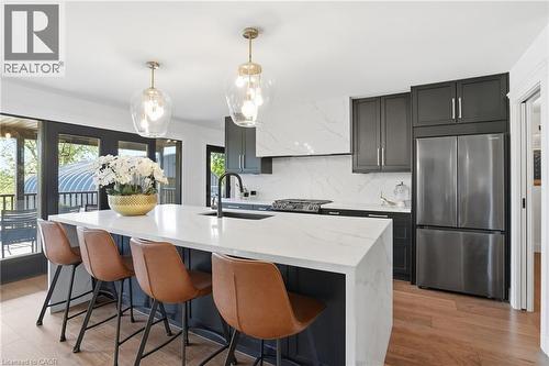 Modern kitchen featuring a large waterfall island with integrated sink, black cabinetry, stainless steel appliances, and wood-finish flooring - 71 Miles Road, Hamilton, ON 