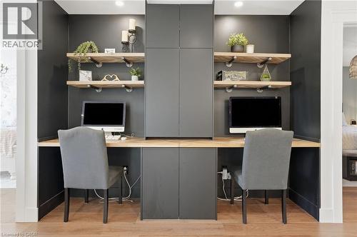Dedicated dual workspace featuring built-in cabinetry, floating wood shelves with industrial-style brackets, a continuous wood-finish countertop, and recessed lighting - 71 Miles Road, Hamilton, ON 