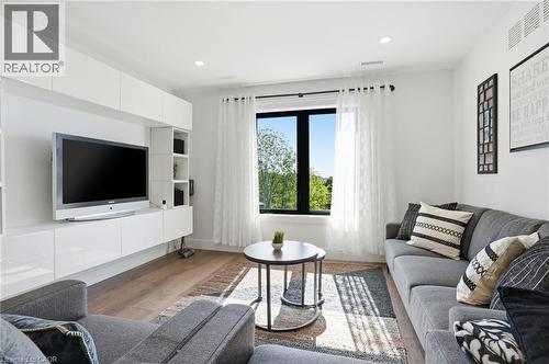 Light-filled living area featuring wood-finish flooring, a contemporary built-in media console with glossy white cabinetry, and a prominent window with dark framing - 71 Miles Road, Hamilton, ON 