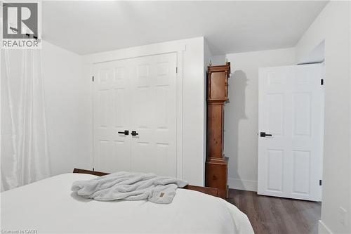 Interior space featuring wood-finish flooring, white paneled doors with black hardware, and ample natural light from a window with sheer white curtains - 71 Miles Road, Hamilton, ON 