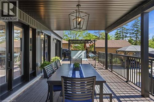 Expansive covered deck featuring composite decking, black metal railings, and a contemporary geometric pendant light - 71 Miles Road, Hamilton, ON 