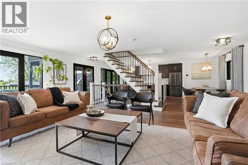 Open-concept living area featuring wood-finish flooring, a contemporary staircase with dark metal balusters, and multiple large glass panel doors - 71 Miles Road, Hamilton, ON 