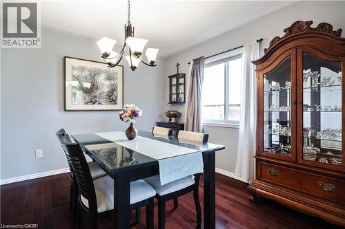 Dining area featuring dark wood-finish flooring, a contemporary chandelier, a large window with white trim, and a display cabinet with glass doors - 106 Moore Crescent, Ancaster, ON 