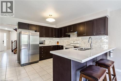 Kitchen featuring dark wood-finish cabinetry, light-toned countertops, and a full-height honeycomb tile backsplash - 106 Moore Crescent, Ancaster, ON 