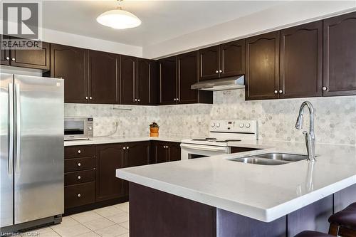 Kitchen featuring dark wood cabinetry, light countertops, honeycomb tile backsplash, stainless steel refrigerator, and a double basin sink with a gooseneck faucet - 106 Moore Crescent, Ancaster, ON 