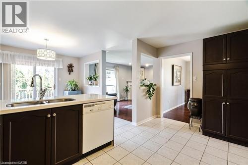 Kitchen island featuring an undermount stainless steel sink with gooseneck faucet, light-toned countertop, and integrated dishwasher - 106 Moore Crescent, Ancaster, ON 
