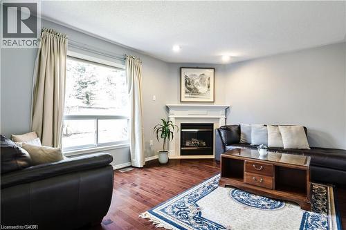 Living area featuring rich wood-finish flooring, a prominent fireplace with a classic mantelpiece, and a large window providing ample natural light - 106 Moore Crescent, Ancaster, ON 