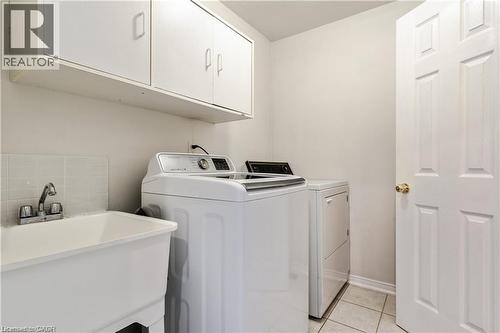 Utility room featuring a laundry pair, wall-mounted cabinetry, a utility sink with a chrome faucet, and tiled flooring - 106 Moore Crescent, Ancaster, ON 