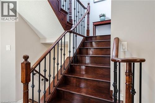 Staircase with rich wood-finish treads and risers, featuring decorative black wrought iron spindles and a matching wood-finish handrail - 106 Moore Crescent, Ancaster, ON 