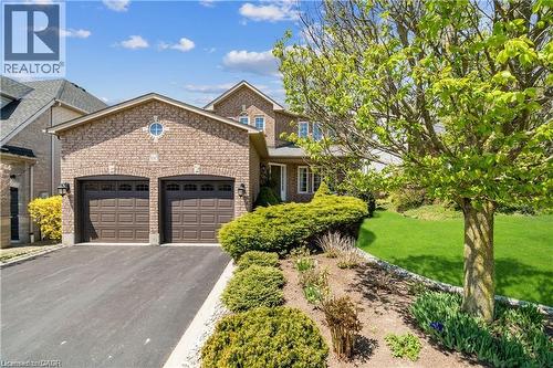 Brick facade residence featuring an attached two-car garage with panel doors, a circular window accent, and a paved driveway - 106 Moore Crescent, Ancaster, ON 