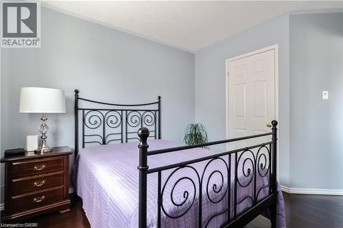 Bedroom featuring dark wood-finish flooring, light blue wall paint, white trim, and a white paneled door - 106 Moore Crescent, Ancaster, ON 