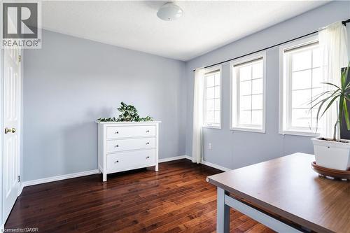 Room featuring rich wood-finish flooring, light blue wall paint, and three large windows with white trim - 106 Moore Crescent, Ancaster, ON 