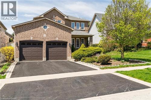 Brick facade residence featuring a two-car garage with arched panel doors, a circular window accent, and established front landscaping - 106 Moore Crescent, Ancaster, ON 