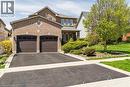 Brick facade residence featuring a two-car garage with arched panel doors, a circular window accent, and established front landscaping - 106 Moore Crescent, Ancaster, ON 