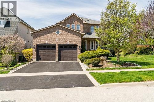 Brick facade residence featuring a two-car garage, asphalt driveway, mature trees, manicured front lawn, and foundational landscaping - 106 Moore Crescent, Ancaster, ON 