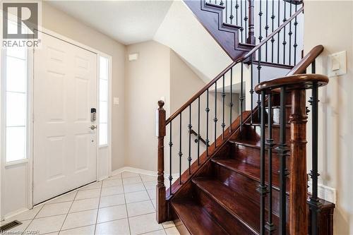 Entryway featuring a white door with sidelights, tiled flooring, wood-finish staircase, and wrought iron balusters - 106 Moore Crescent, Ancaster, ON 