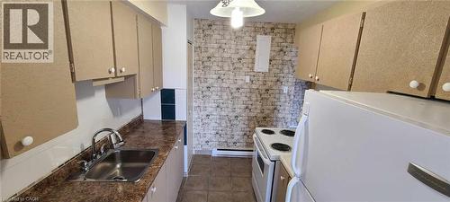 Galley kitchen featuring light brown cabinetry, speckled countertops, a stainless steel sink with a chrome faucet, white appliances, and a brick-patterned accent wall - 105 Conroy Crescent Unit# 505, Guelph, ON 