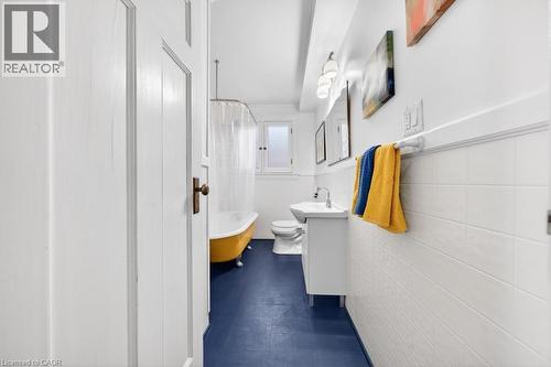 Bathroom featuring a yellow clawfoot tub, white tile wainscoting, and a single-pane window - 35 Burris Street, Hamilton, ON - Indoor