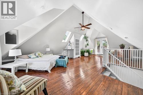 Spacious attic conversion featuring vaulted ceilings, rich wood-finish flooring, white spindle railing, and a pair of French doors opening to an exterior balcony - 35 Burris Street, Hamilton, ON - Indoor