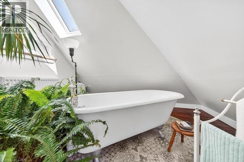 Freestanding bathtub with claw feet, set against an angled ceiling and patterned floor tiles - 35 Burris Street, Hamilton, ON - 
