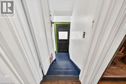 Staircase featuring painted treads and risers, with white paneled walls and a contrasting dark door with a transom window - 35 Burris Street, Hamilton, ON - Indoor Photo Showing Other Room