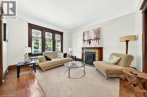 Living room featuring hardwood flooring, a decorative fireplace with a patterned tile surround, and a large window with stained glass accents - 35 Burris Street, Hamilton, ON - Indoor Photo Showing Living Room With Fireplace