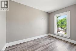 Room featuring a single window with view into backyard, light gray walls, white baseboards, and wood-finish flooring - 