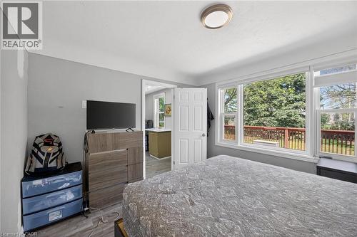 Bedroom featuring a large window overlooking a wooden deck and exterior greenery, light gray painted walls, wood-finish flooring, and a flush mount ceiling light fixture - 43 West 1St Street, Hamilton, ON 