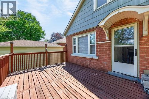 Outdoor wood deck with a full wooden railing, a brick exterior wall, a white-framed window, and a white storm door with an arched decorative awning - 43 West 1St Street, Hamilton, ON 