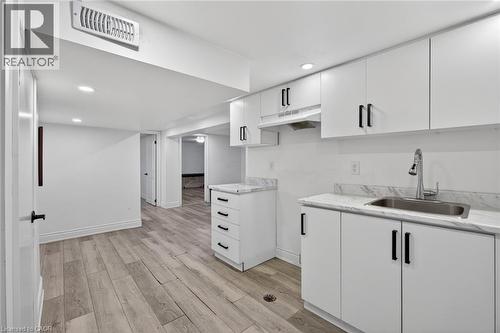 Contemporary kitchen area featuring white cabinetry with black hardware, a stainless steel sink, and light-toned, wood-finish flooring - 43 West 1St Street, Hamilton, ON 