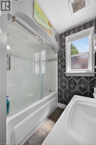 Bathroom featuring patterned accent wall, a white tub with sliding glass doors, white subway tile surround, and a white sink - 43 West 1St Street, Hamilton, ON 