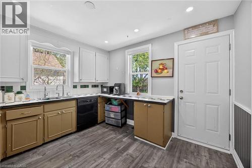Kitchen featuring wood-finish flooring, two large windows, white upper cabinetry, and a stainless-steel sink with a modern faucet - 43 West 1St Street, Hamilton, ON 