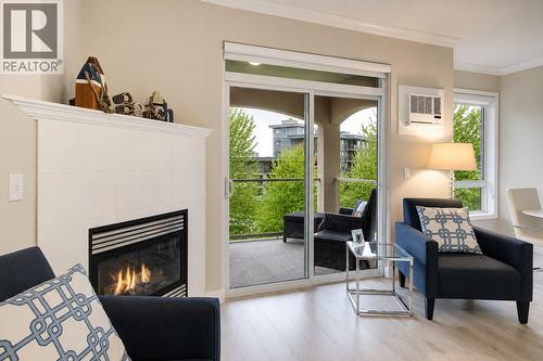 Living room with gas fireplace and access to spacious covered deck. (digitally altered photos – leaves added) - 1960 Enterprise Way Unit# 412, Kelowna, BC - Indoor Photo Showing Living Room With Fireplace