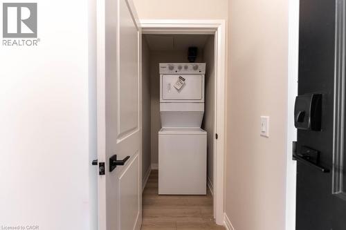 Washroom with estacked washer and dryer and light wood-style floors - 120 Springvalley Crescent Unit# 104, Hamilton, ON 