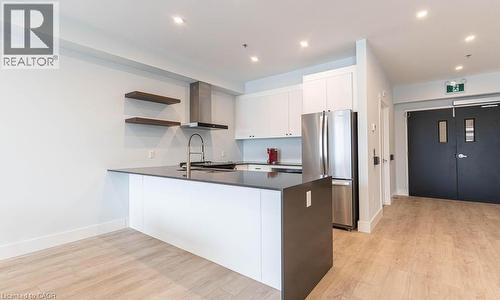 Kitchen featuring open shelves, a peninsula, freestanding refrigerator, wall chimney range hood, and light wood-type flooring - 120 Springvalley Crescent Unit# 104, Hamilton, ON 