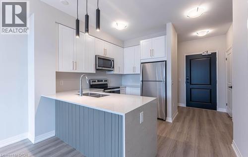 Kitchen featuring appliances with stainless steel finishes, white cabinets, a peninsula, pendant lighting, and light stone countertops - 120 Springvalley Crescent Unit# 104, Hamilton, ON 