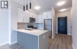 Kitchen featuring appliances with stainless steel finishes, white cabinets, a peninsula, pendant lighting, and light stone countertops - 