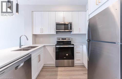 Kitchen with stainless steel appliances, white cabinetry, and light wood finished floors - 120 Springvalley Crescent Unit# 104, Hamilton, ON 