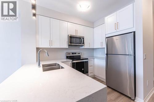 Kitchen with stainless steel appliances, light stone countertops, white cabinets, and light wood-type flooring - 120 Springvalley Crescent Unit# 104, Hamilton, ON 