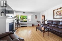 Bright living area featuring wood-finish flooring, a white mantel fireplace with a dark hearth, and a large multi-pane window with a window seat - 