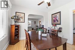 Dining area featuring wood-finish flooring, a ceiling fan with light fixture, and an arched doorway opening to an additional room - 