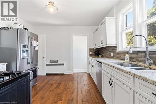 Kitchen featuring wood-finish flooring, white cabinetry with dark hardware, stone countertops, and a mosaic tile backsplash - 134 Queensway Drive, Brantford, ON 