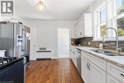 Kitchen featuring wood-finish flooring, white cabinetry with dark hardware, stone countertops, and a mosaic tile backsplash - 
