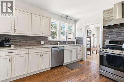 Kitchen featuring white cabinetry, granite countertops, a horizontal stacked tile backsplash, stainless steel appliances, and wood-finish flooring - 134 Queensway Drive, Brantford, ON 