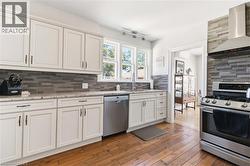 Kitchen featuring white cabinetry, granite countertops, a horizontal stacked tile backsplash, stainless steel appliances, and wood-finish flooring - 