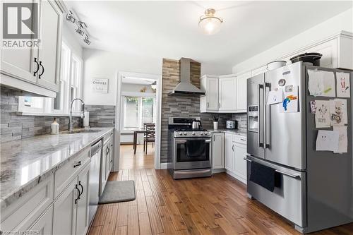 Kitchen featuring shaker-style white cabinetry, stainless steel appliances, a stacked stone backsplash, wood-finish flooring, and light-toned countertops - 134 Queensway Drive, Brantford, ON 