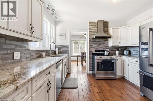 Modern kitchen featuring white cabinetry, stone countertops, a mosaic tile backsplash, stainless steel appliances, and wood-finish flooring - 134 Queensway Drive, Brantford, ON 