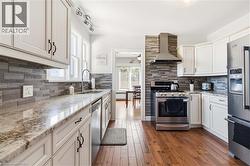 Modern kitchen featuring white cabinetry, stone countertops, a mosaic tile backsplash, stainless steel appliances, and wood-finish flooring - 