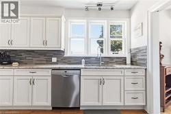 Kitchen featuring white shaker cabinetry, stone countertops, a tiled backsplash, stainless steel dishwasher, and a window above the sink - 