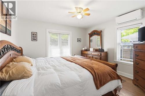 Bedroom featuring light gray walls, wood-finish flooring, a ceiling fan with integrated lighting, a ductless mini-split system, and a window with blinds - 134 Queensway Drive, Brantford, ON 